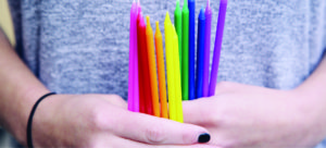 Hands holding rainbow candles